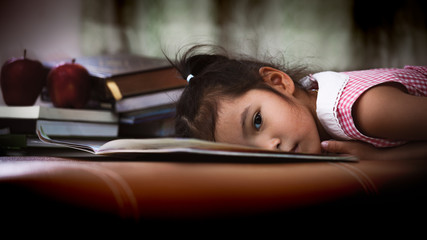 Child asian little girl is lying down on book and bored to read a book in dark tone