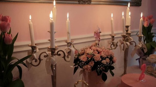 Burning candles, bouquets of flowers on table in banquet hall. Bouquet from miniature pink roses set of lob in stylish candlesticks with ribbons and sweety cake stand on large desk of buffet table