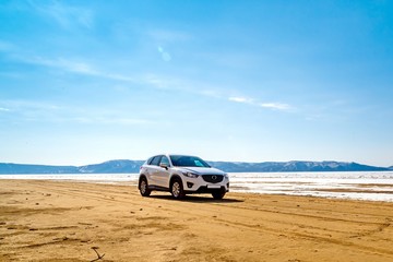 A white car in the spring on a sandy beach in front of a river, mountains, melting ice