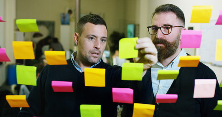 Two creative and thoughtful in a creative agency with colored and planning notes hanging from the...