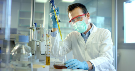 nice young scientist male doctor analyzing liquids virus cells in professional laboratory using qualified equipment and wearing glasses to protect eyes and taking care of the lab glasses