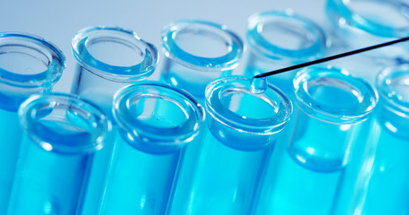 In a laboratory, a scientist with a pipette analyzes a colored liquid to extract the DNA and molecules in the test tubes. Concept: research, biochemistry, nature, pharmaceutical medicine	