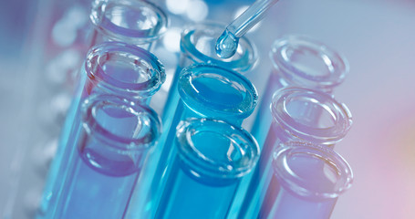 In a laboratory, a scientist with a pipette analyzes a colored liquid to extract the DNA and molecules in the test tubes. Concept: research, biochemistry, nature, pharmaceutical medicine	
