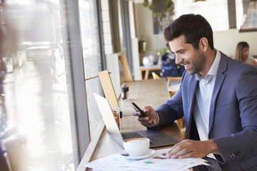 Businessman Using Phone Whilst Working In Coffee Shop