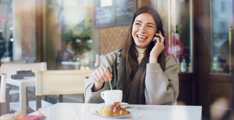 One morning a beautiful elegant woman eats breakfast at the outdoor cafe with a coffee and croissants while reading the news or emails on his tablet. Concept: Breakfast, relax, coffee, business.	