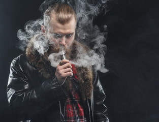 Vaping man holding a mod. A cloud of vapor. Black background. Studio shooting.