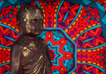 Buddha statue on a colorful background / featuring a wooden statue of  cheerful wise Buddha on colorful Oriental artistic pattern background