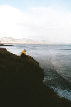 Person sitting by the sea on a cliff