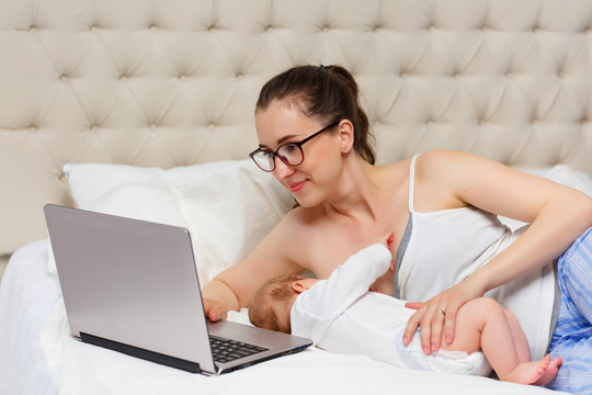 Portrait of a beautiful mother breastfeeding her 3-month-old child in the bedroom, working at a computer, side view, the concept of breastfeeding and work