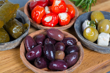 Mediterranean appetizer antipasti tapas bowls with green and calamata olives, feta cheese, stuffed pepper, herbs on wooden plank