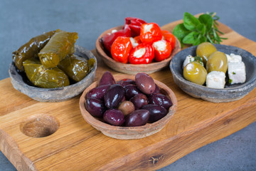 Mediterranean appetizer antipasti tapas bowls with green and calamata olives, feta cheese, stuffed pepper, herbs on wooden plank