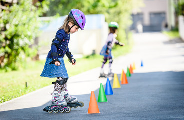 Children learning to roller skate on the road with cones.
