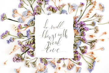 Inspirational quote "Do small things with great love" written in calligraphic style on paper with blue and purple dried flowers on white background. Flat lay, top view