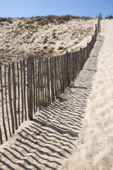 Wooden fence and his shadows on the sand on an Atlantic coastline in France