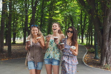 Three beautiful young girls eat donuts in park.