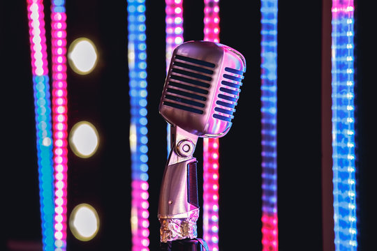 Retro style microphone on stage in the spotlight performance of the musical group. Microphone for rock music. Microphone in blue light og stage. Music is in the air. Color background.