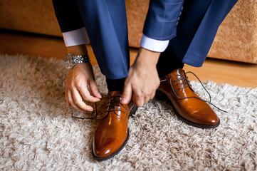 A man ties up his shoelaces on his brown shoes in the room. - obrazy, fototapety, plakaty