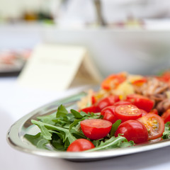 Salad of tomato greens and seafood on a white table.