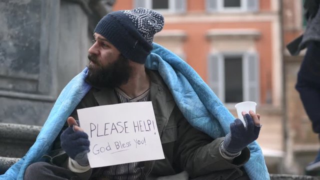 portrait of homeless sitting in the street receives a coin from a person