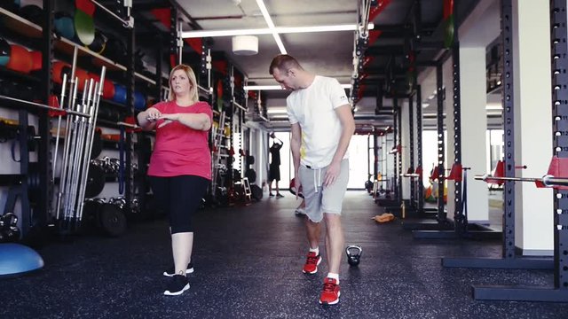 Overweight woman with personal trainer in modern gym.