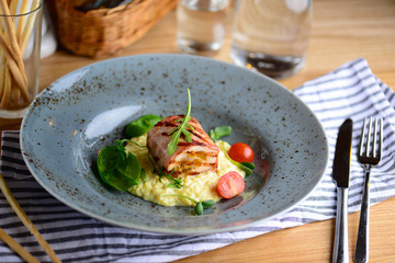 Juicy chicken roll with risotto, cherry tomatoes and greenery on a plate served for a dinner in a restaurant. Tasty food concept.