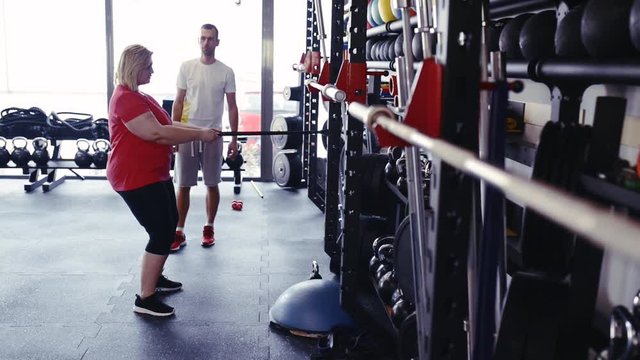 Overweight woman in gym training arms with trx fitness strips.