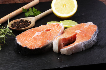 Fresh raw salmon fish steaks with fresh herbs on stone background