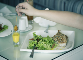 Fish with a salad in a plate is servered on a table with a glass of carrot juice. The female is having lunch.