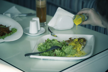 Fish with a salad in a plate is servered on a table with a glass of carrot juice. The female is having lunch.