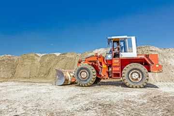 Bulldozer is making pile of soil by pulling ground up on heap at construction site, project in...