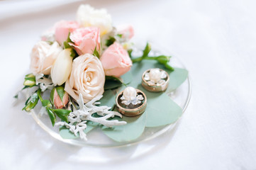 On a plate are wedding rings, earrings and flowers roses.