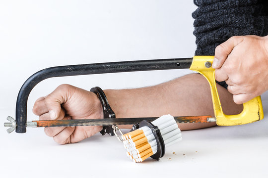 Cigarettes and hand of a man in handcuffs. The man sawing the cuffs. Isolated on a white background.