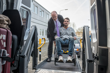 Cab Driver Assisting Disabled Man To Board Wheelchair Lift Van