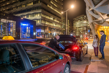 Driver Loading Passenger Luggage In Car Trunk On Street