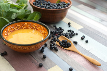 Bowl of honey next to the leaves of green mint and blueberries in a clay bowl