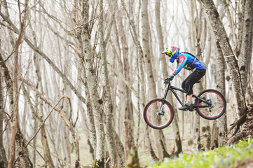 A mountain bike rider jumps from a springboard in a foggy forest, in the Caucasus Mountains