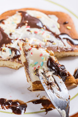 Slice of american pancake topped with chocolate cream and sprinkles on the fork closeup macro