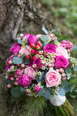 Close-up of pink roses wedding bouquet placed outdoors next to a tree trunk