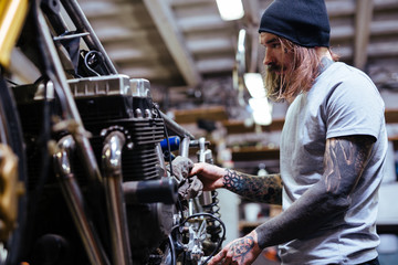 Side view portrait of tattooed man working in garage repairing broken motorcycle and customizing it