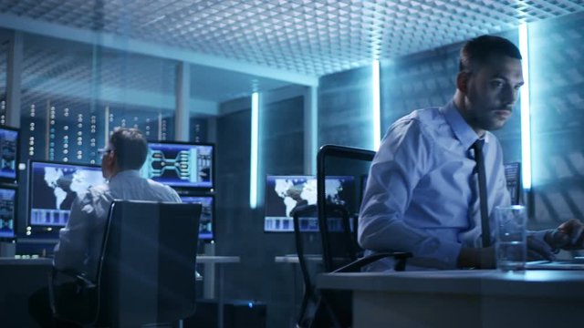 Two Technical Engineers at Sitting at Their Workplaces With Multiple Displays. They're in Monitoring Room with Servers.  Shot on RED EPIC-W 8K Helium Cinema Camera.