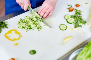 Hands of young trainee with knife cutting fresh cucumbers