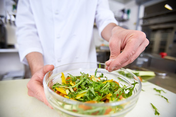 Chef adding pinch of salt into vegetarian salad