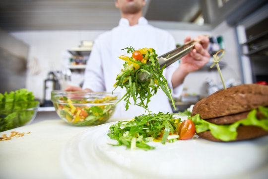 Chef putting fresh vegetable salad on plate for client