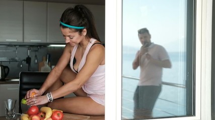 Young woman squeezes orange juice sitting by window in kitchen. Sweet brunette in pink body with bare legs coquettishly settled on table on which stand juicer and fruit. Fascinated by process of - Powered by Adobe