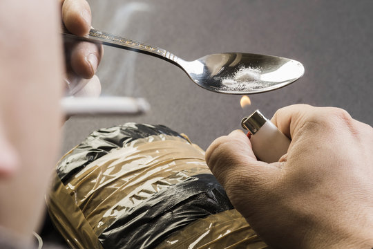 The use of illegal drugs, drugs. A man preparing heroin, using a spoon and a lighter.