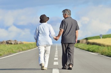 手をつないで一本道を歩くシニアの日本人夫婦