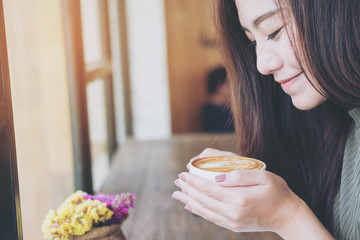 A beautiful asian woman holding and smelling hot coffee cup in loft cafe with feeling happy and smiley face