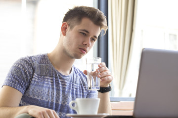 Young man sits, looks at the laptop and surf the internet