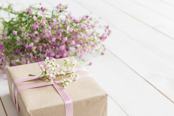 White wooden table with pink flowers and a present, mother's day concept