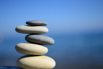 Fototapeta na wymiar Zen spa stones with blue water and sky. Balanced stones background, copy space. Spa symbol. Balancing stones. Symbol of stability. Tranquil, relaxation and health life. Stones balance. Sustainability.